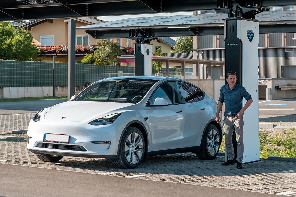 Mann steht neben Tesla unter einem Solarcarport mit Ladesäule